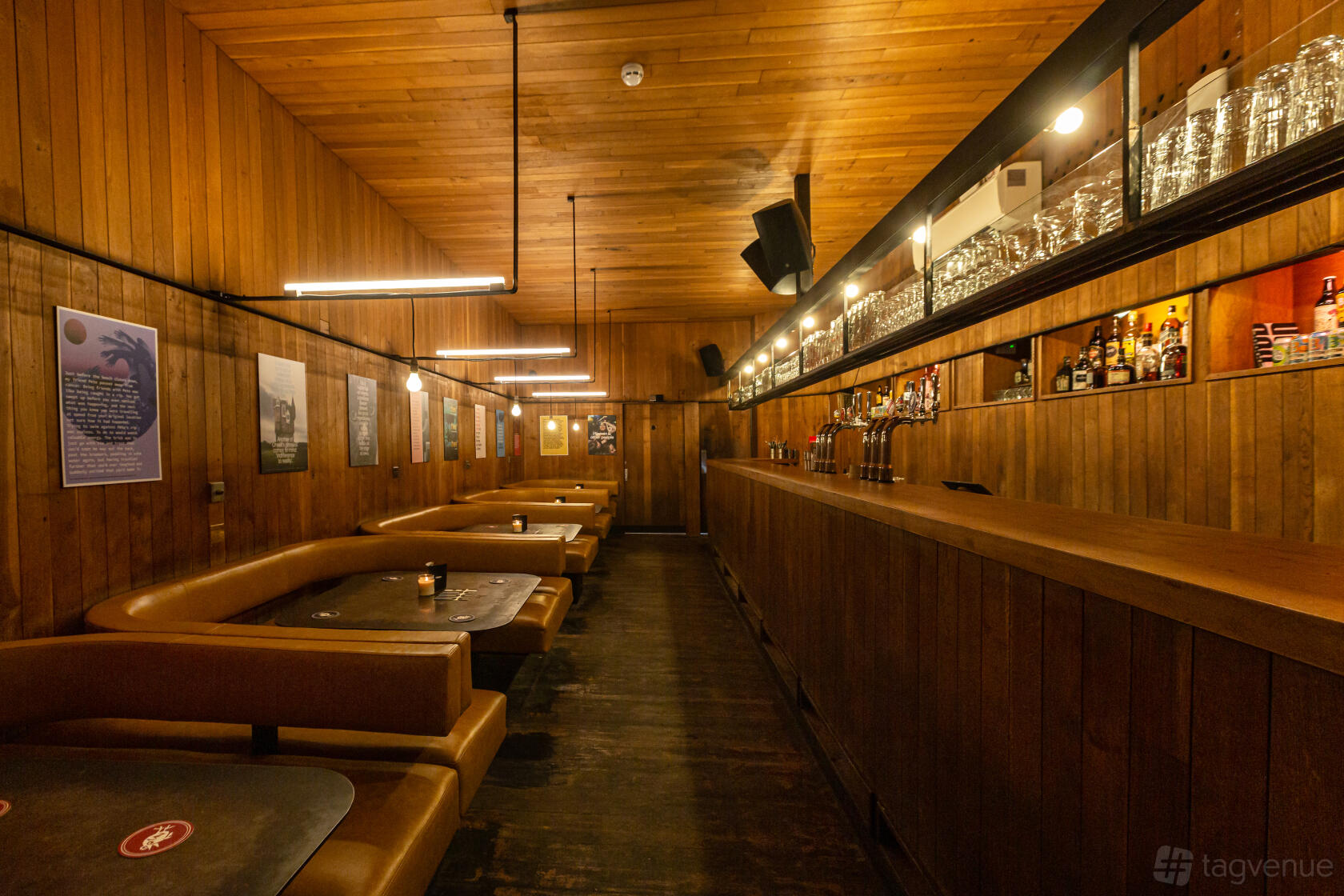 A bar with wood-paneled walls, booth seating, overhead pendant lights, and a long counter at The Social.