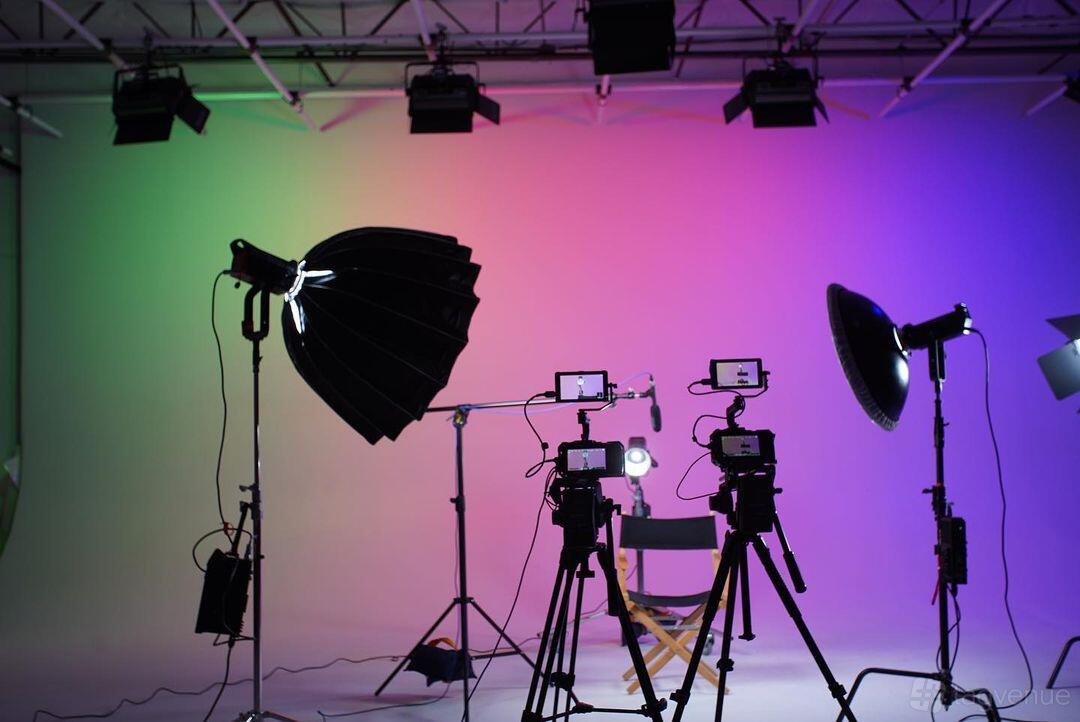 A photo and film studio with a colorful gradient backdrop, studio lights, and cameras on tripods at Camera Ready Studios.