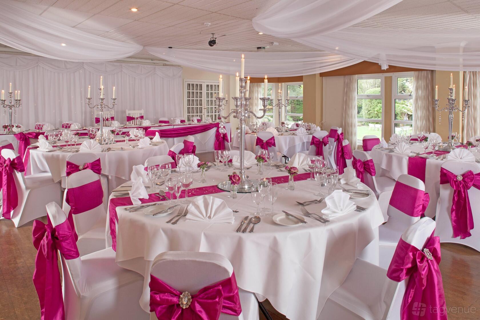 An event space with round tables set with white linens, pink chair sashes, and tall candelabras at The Abbey Sands Hotel.