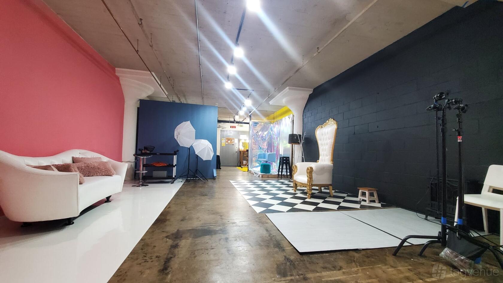 A photo studio with colored feature walls, softbox lighting, a white sofa, and a throne chair at LTE Studio Space.