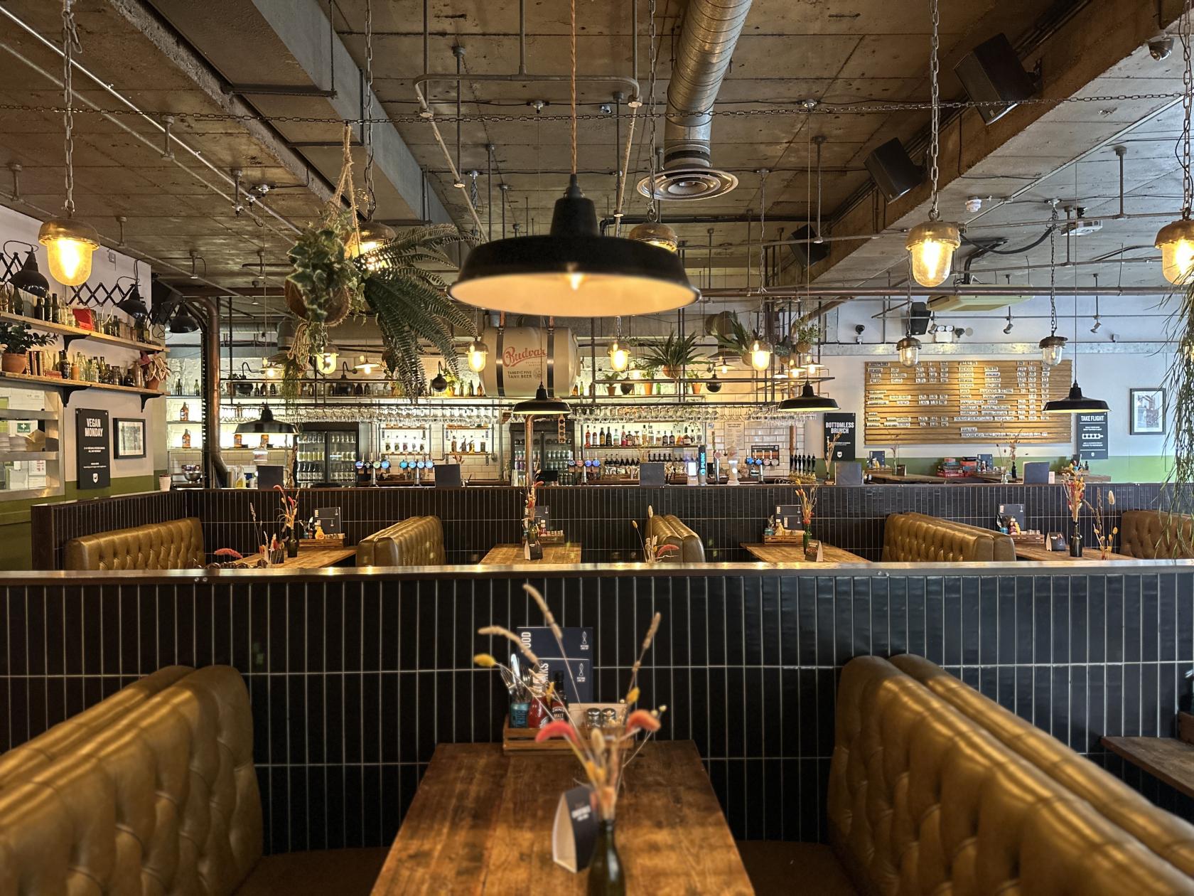 A pub with leather booths, wooden tables, pendant lighting, and a backlit bar at Seething Lane Tap.