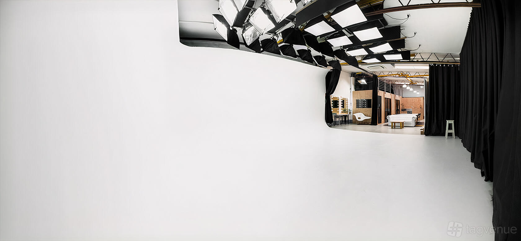 A photo studio with a large white cyclorama wall, overhead lighting, and adjacent makeup stations at Studio Manly.