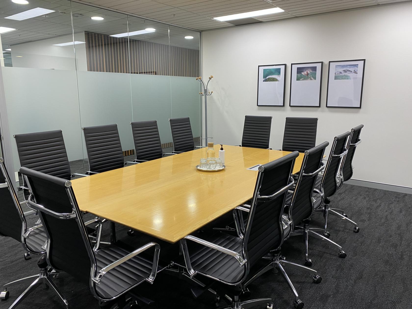 A coworking space with a large wooden conference table, black leather chairs, and framed wall art at Workspace365 Bondi Junction.