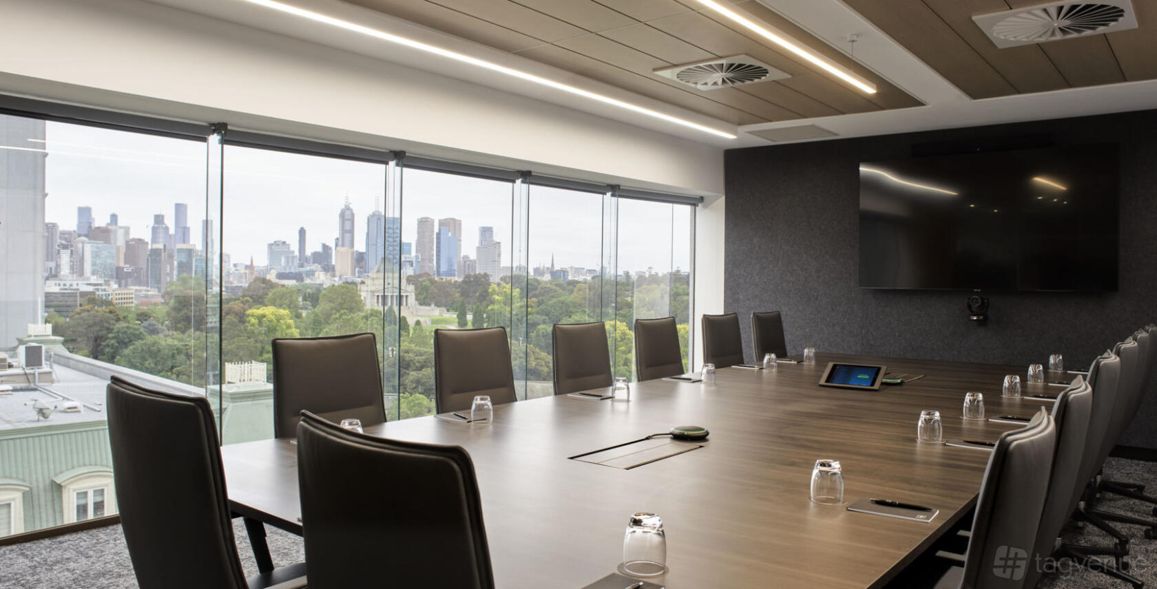 A boardroom with floor-to-ceiling windows, city views, leather chairs, and a wall-mounted screen at Hub St Kilda Road.