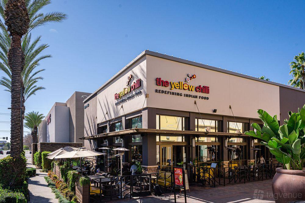 A restaurant terrace with umbrella-shaded tables, outdoor seating, and potted plants at The Yellow Chilli Tustin