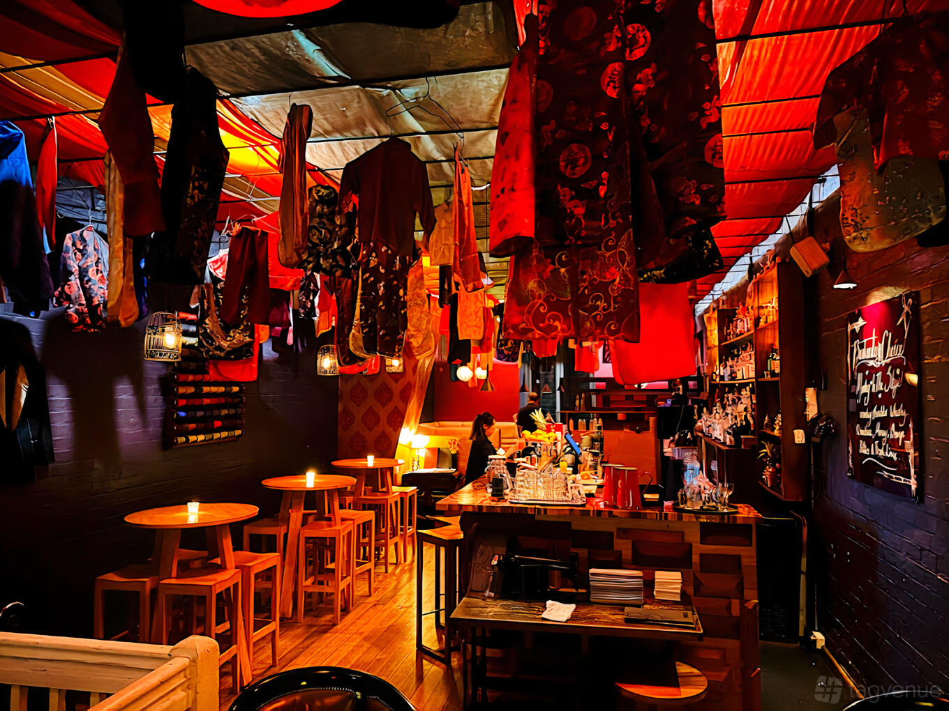 A cocktail bar with hanging red fabric decor, candlelit high tables, and a stocked back bar at Seamstress Restaurant & Bar.