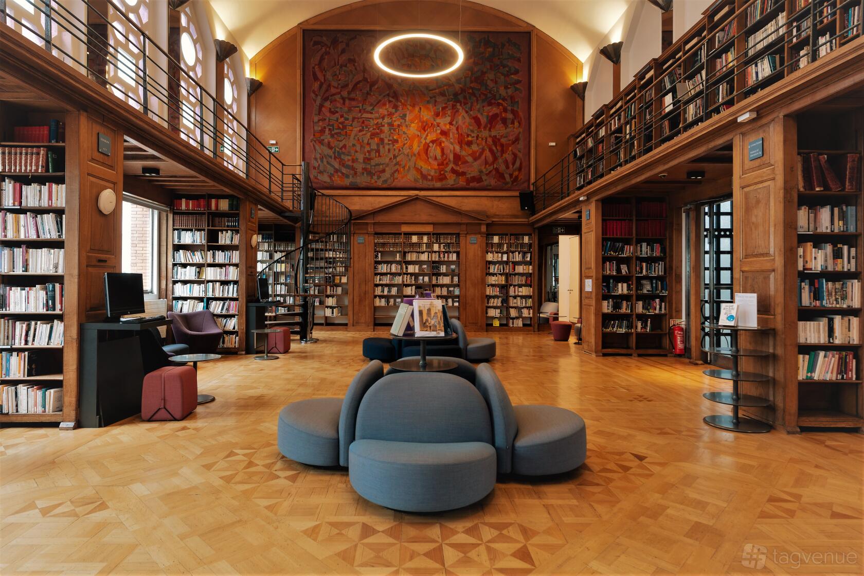 A library with parquet floors, tall wooden bookshelves, an Art Deco mural, and a circular seating area at Institut français au Royaume-Uni.