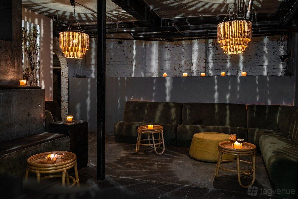 A function room with velvet banquette seating, rattan tables, and chandeliers at The George Lounge.