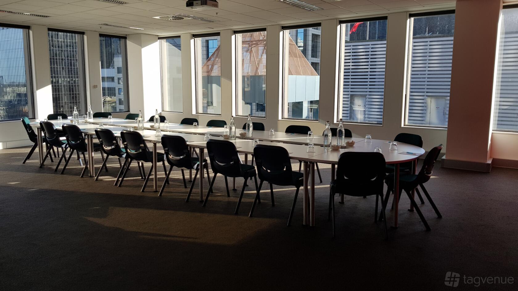 A meeting room with U-shaped tables, black chairs, bottled water, and large windows at Cliftons Melbourne - Collins St.