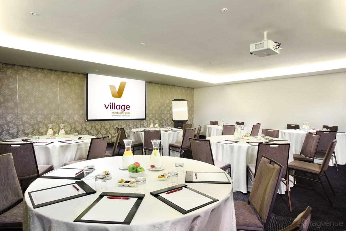 A meeting room with round tables set with stationery, water, and notepads, plus a projector screen at Village Hotel Katong.