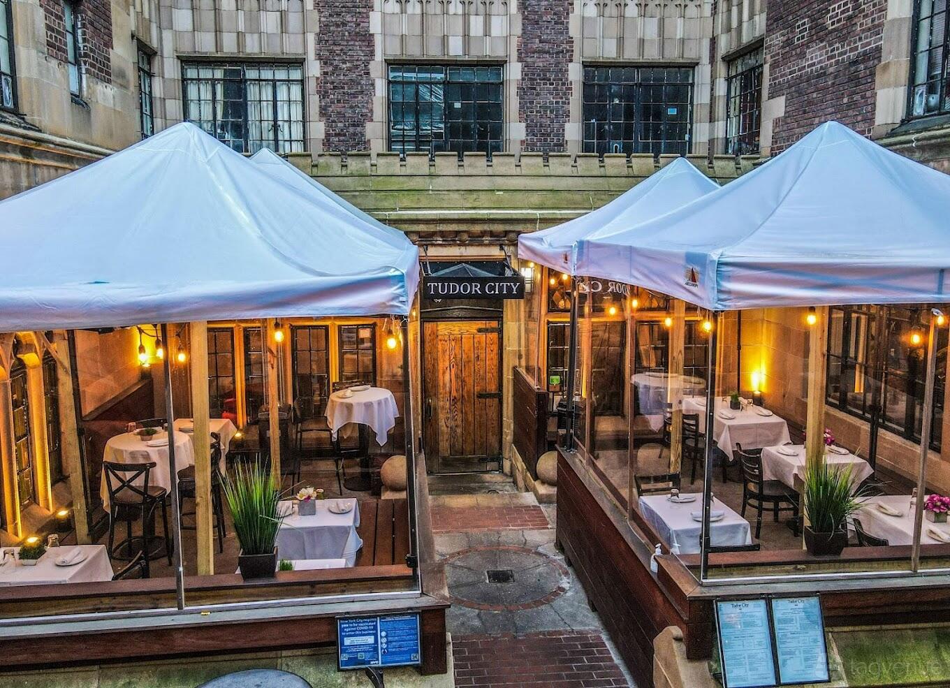 An outdoor restaurant patio with white canopies, string lights, and tables set for dining at Tudor City Steakhouse.