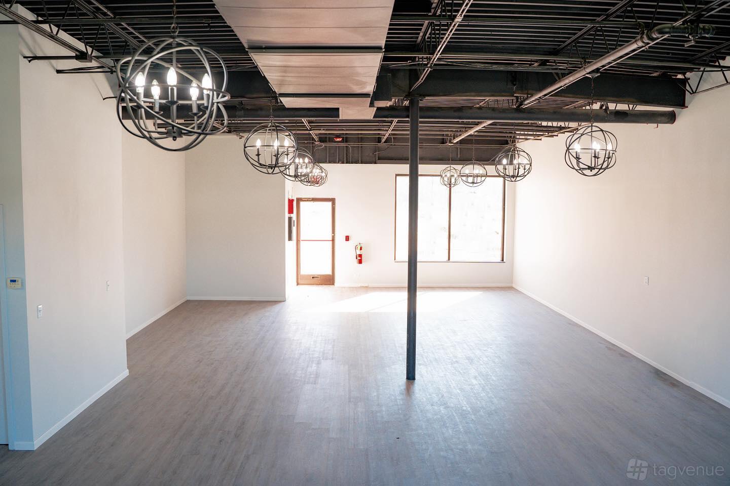 An event venue with polished wood floors, white walls, and round industrial pendant lights at Ave 25 Twelve.