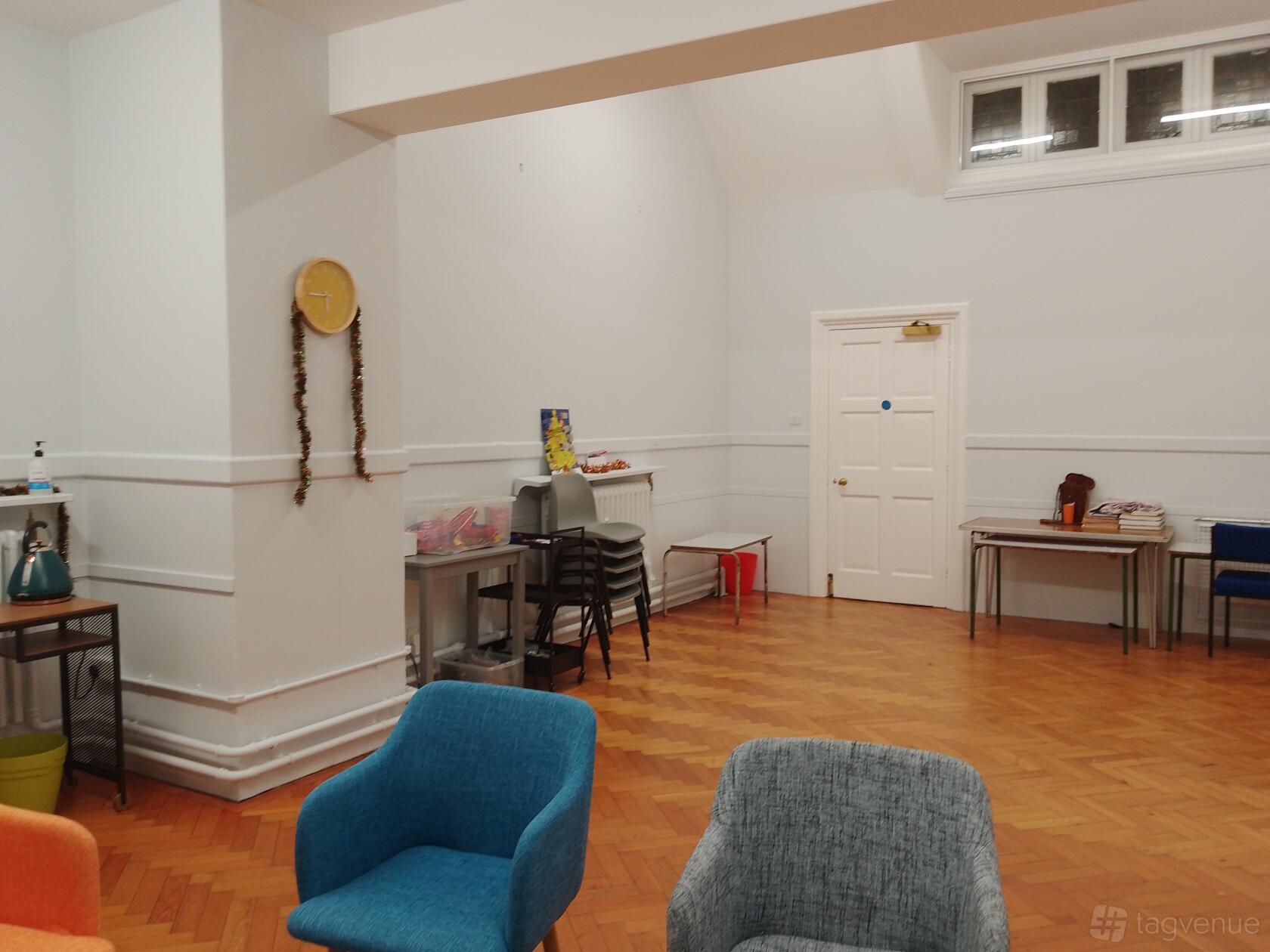 A function room with parquet flooring, colorful chairs, stacked tables, and high ceilings at St Paul's UR Church and halls Croydon.