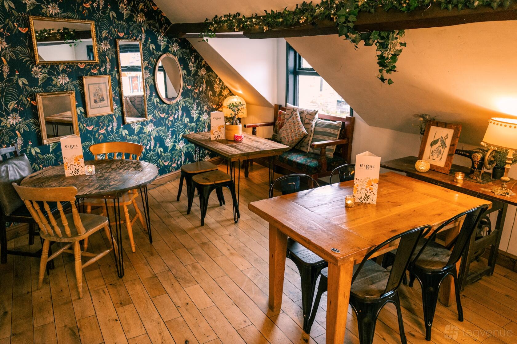 A dining room with wooden tables, mismatched chairs, potted plants, framed art, and natural light at Number 8 Cocktail Bar.
