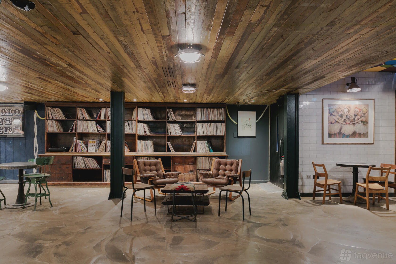 A basement bar with wooden ceiling, vintage armchairs, and a wall of vinyl records at Never For Ever.