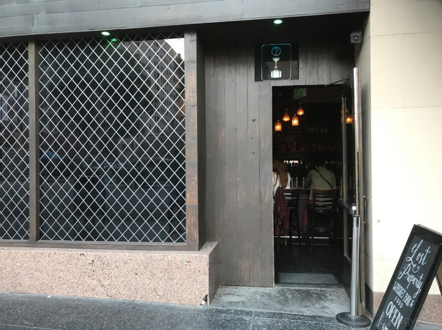 A bar entrance with a wooden door, decorative lattice window, and hanging pendant lights inside at Lost Property Bar.