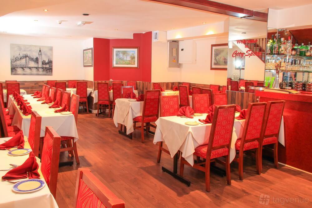 A restaurant with red upholstered chairs, white tablecloths, and a mirrored bar at City Spice.