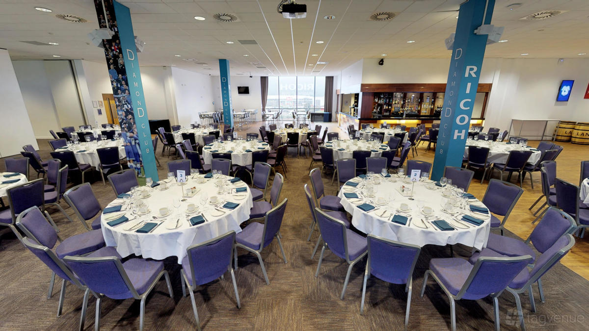 A stadium suite with round tables covered in white linens and blue chairs at Cardiff City Stadium.