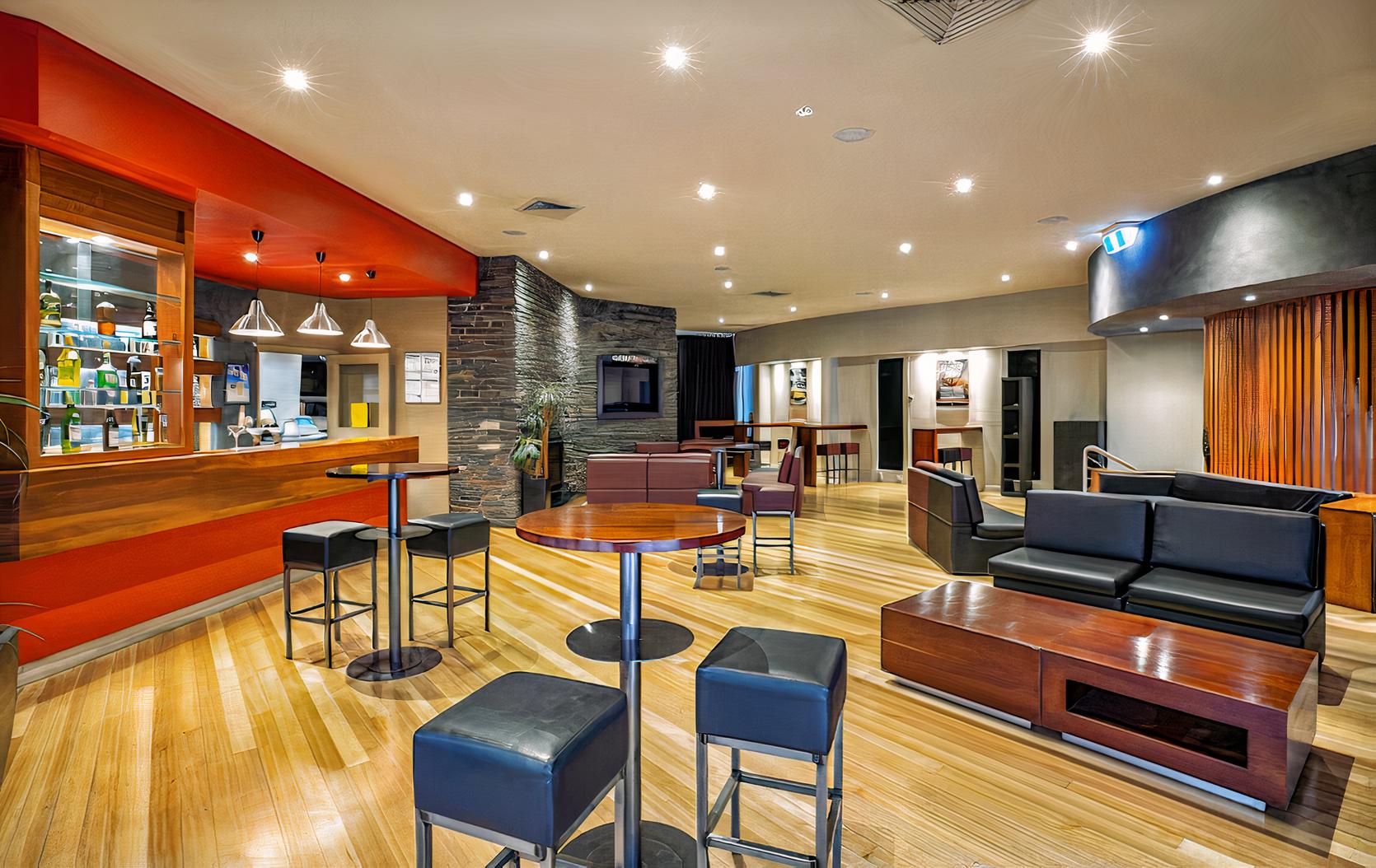 A lounge in a pub with wooden floors, leather seating, high tables with stools, and a bar counter at Vale Hotel.