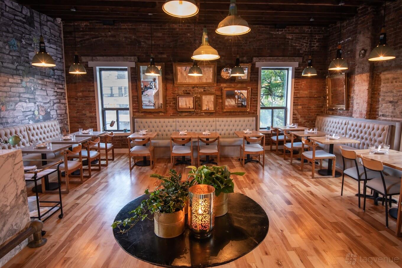 A restaurant with exposed brick walls, tufted banquette seating, and large windows at Nodo Leslieville.
