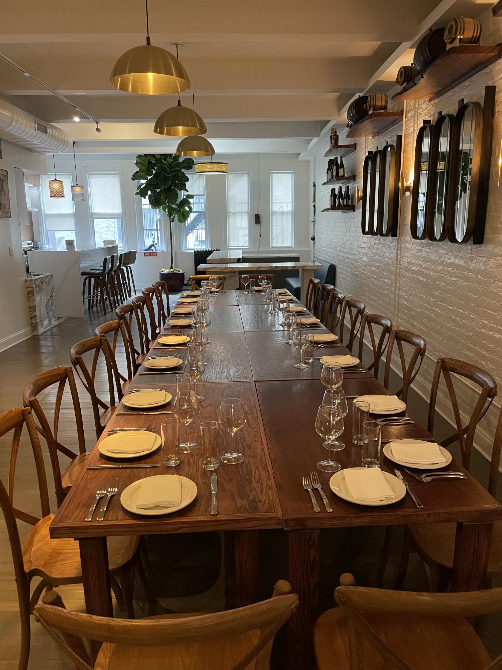 A restaurant with long wooden tables set with plates and glassware, white brick walls, and natural light at The Flatiron Room @ Giorgio's of Gramercy.