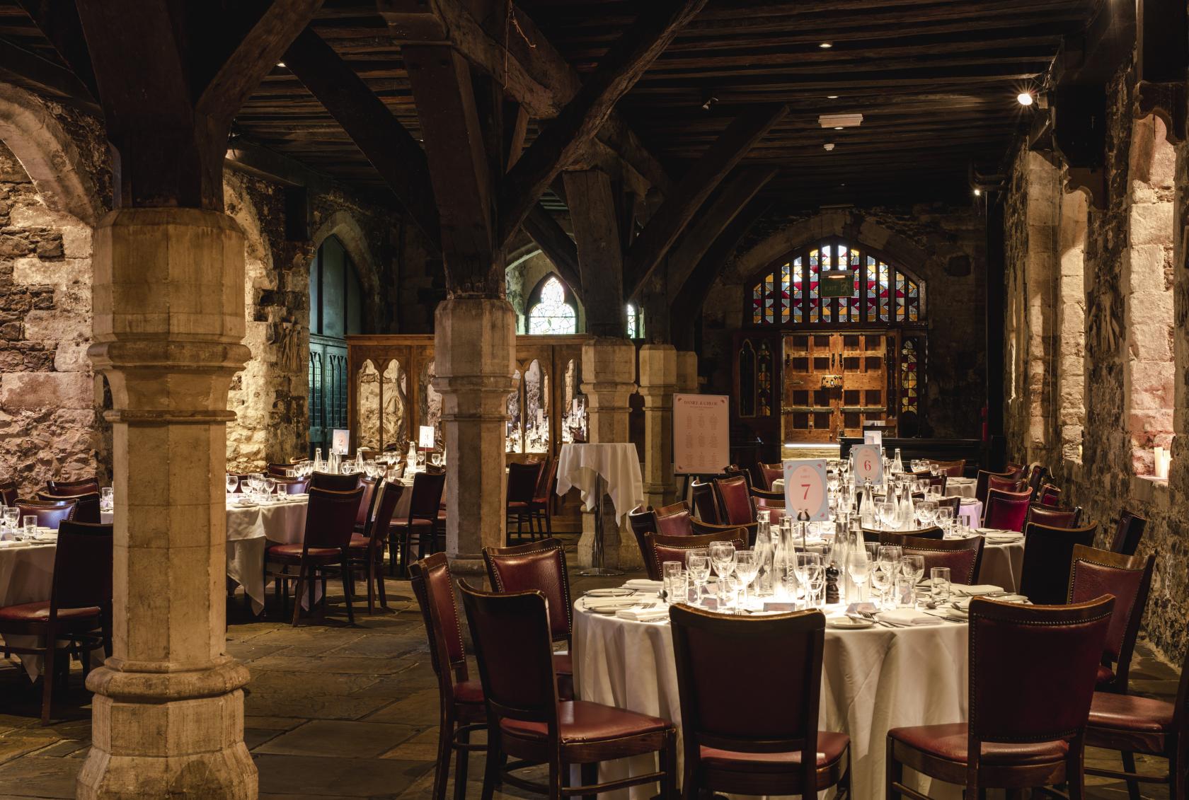 A historic church venue with stone columns, vaulted ceiling, and round tables with white linens at The Crypt.