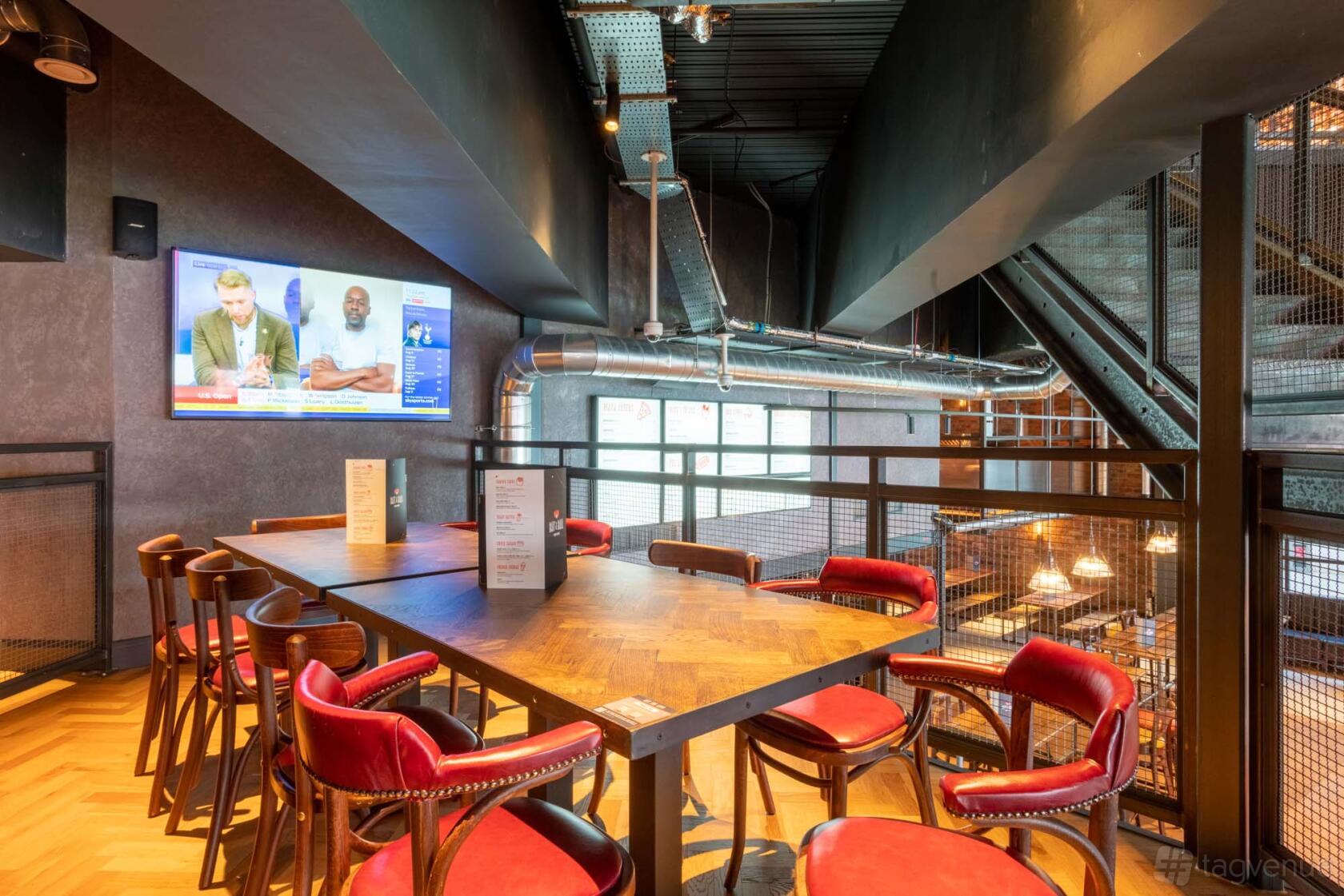 A bar lounge with red velvet chairs, a large screen TV, and exposed ductwork at Bat & Ball.