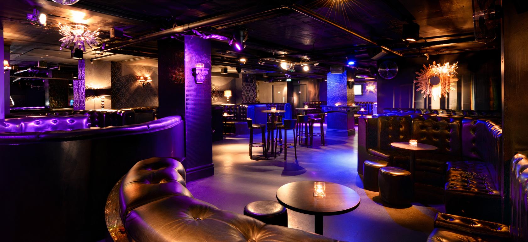 A nightclub event space with tufted leather sofas, high tables, and purple ambient lighting at LUXE.