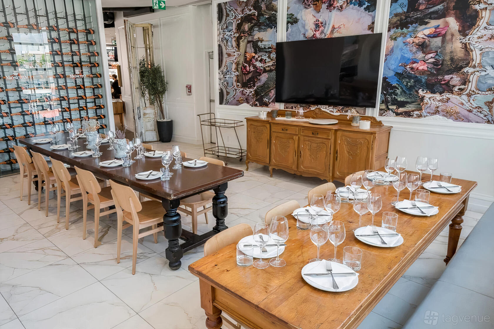 A dining room with two wooden tables set with glassware and a wall-mounted wine rack at Nodo Liberty.