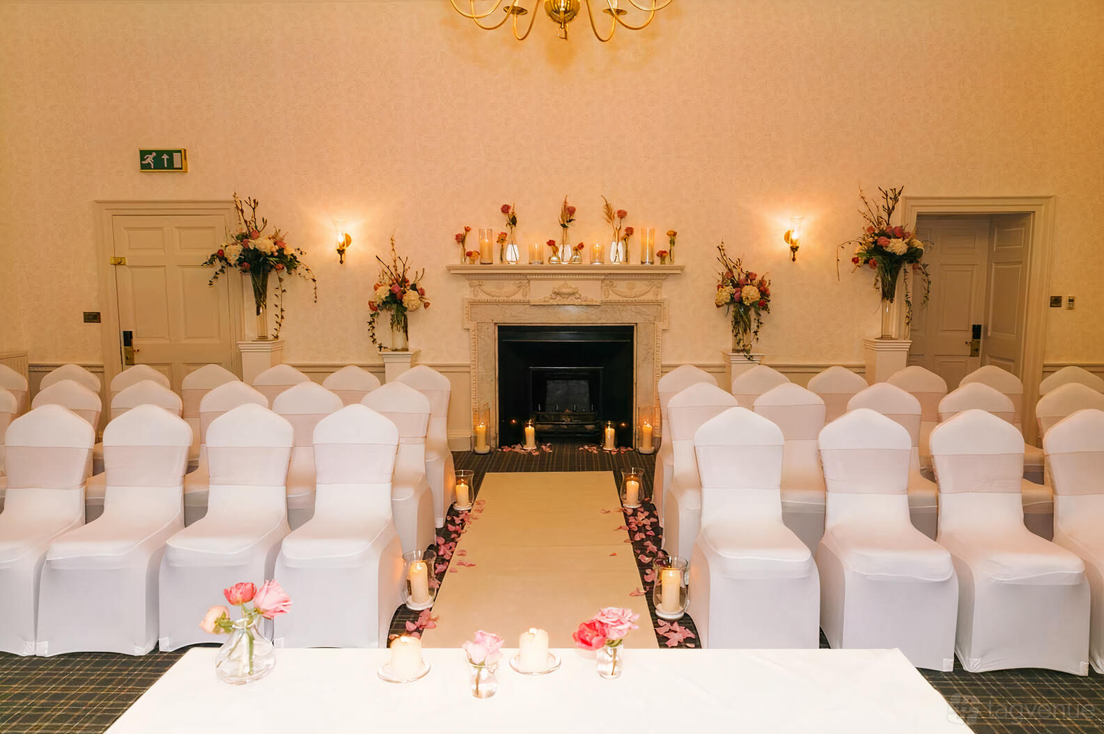 A wedding ceremony setup with white chair covers, aisle candles, and a fireplace in the Wellington Room at Highfield Park.