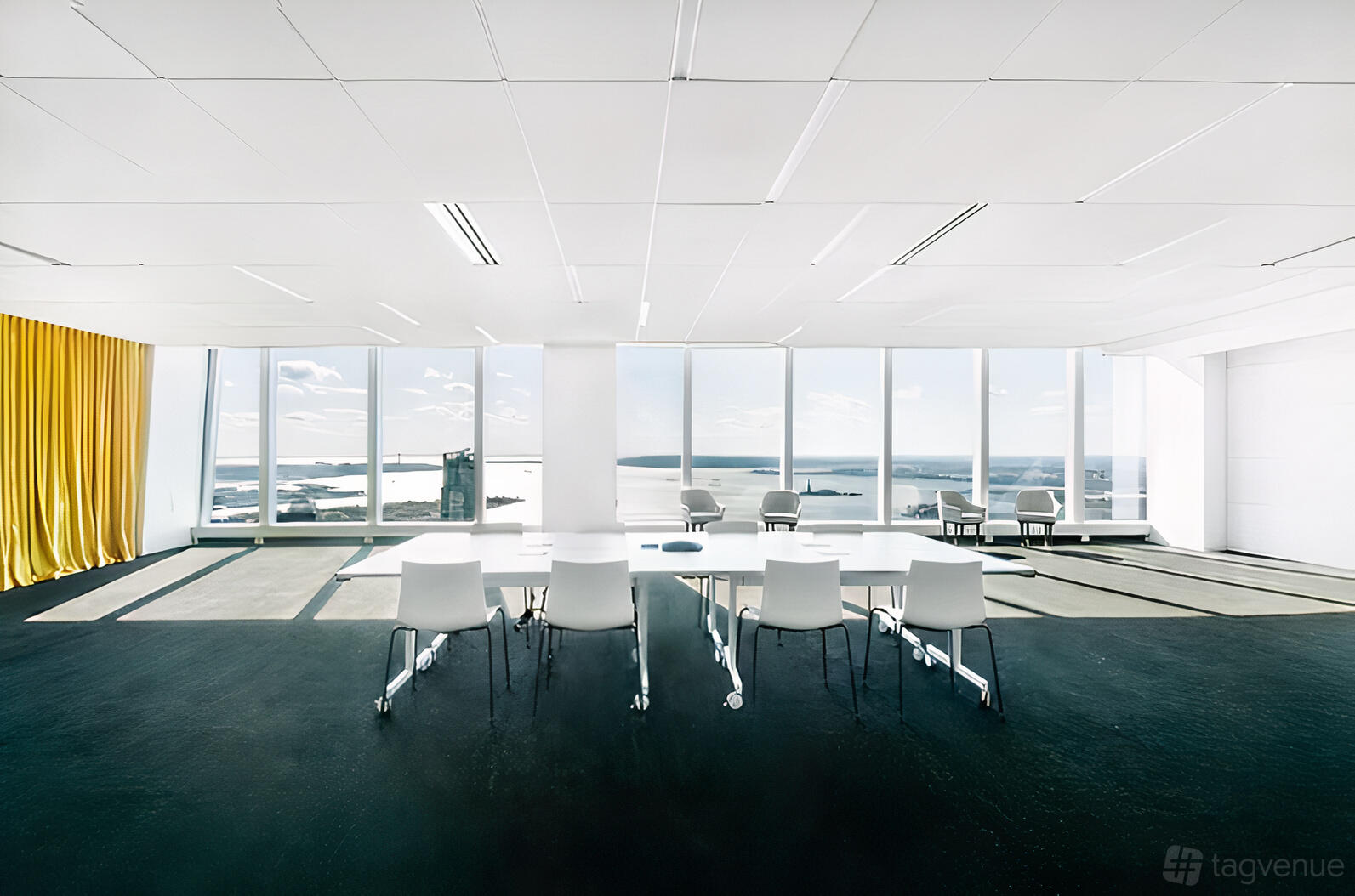 A coworking space with floor-to-ceiling windows, white tables, and yellow curtains at Well& by Durst.