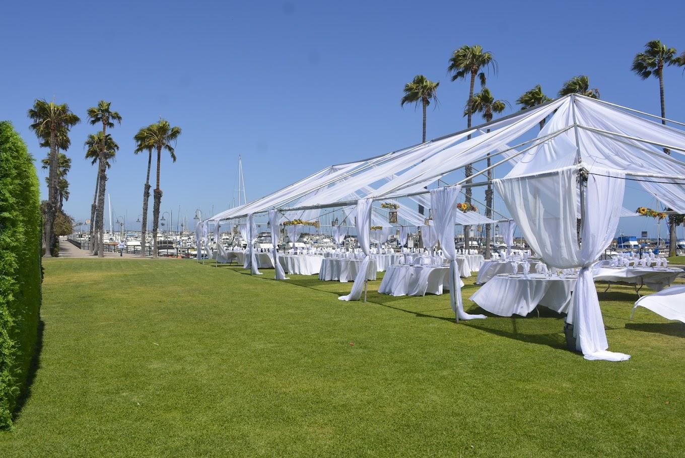 An open air venue with white tent draping, banquet tables, and marina views at The Plaza At Cabrillo Marina.