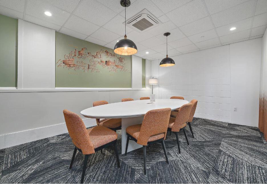 A meeting room with an oval white table, six upholstered chairs, pendant lighting, and mural wall art at 25N Coworking Waco.