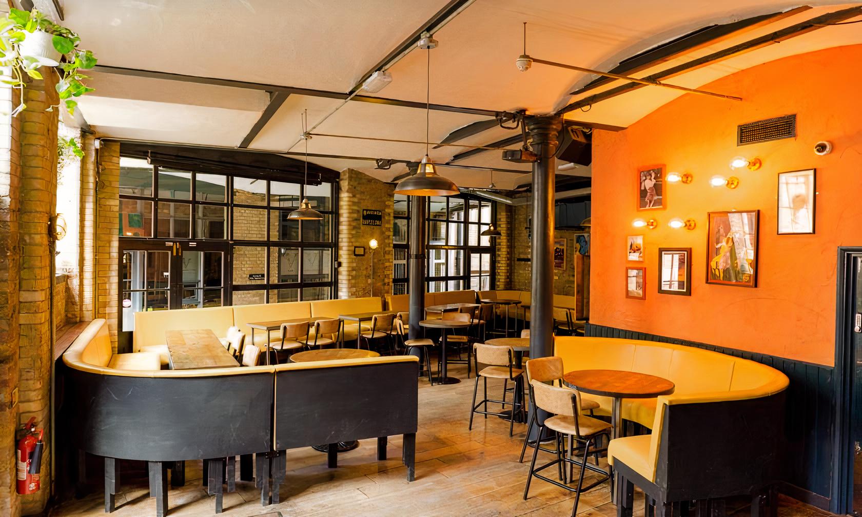 A lounge in a restaurant with curved yellow booths, exposed brick walls, and pendant lighting at Camino King's Cross.