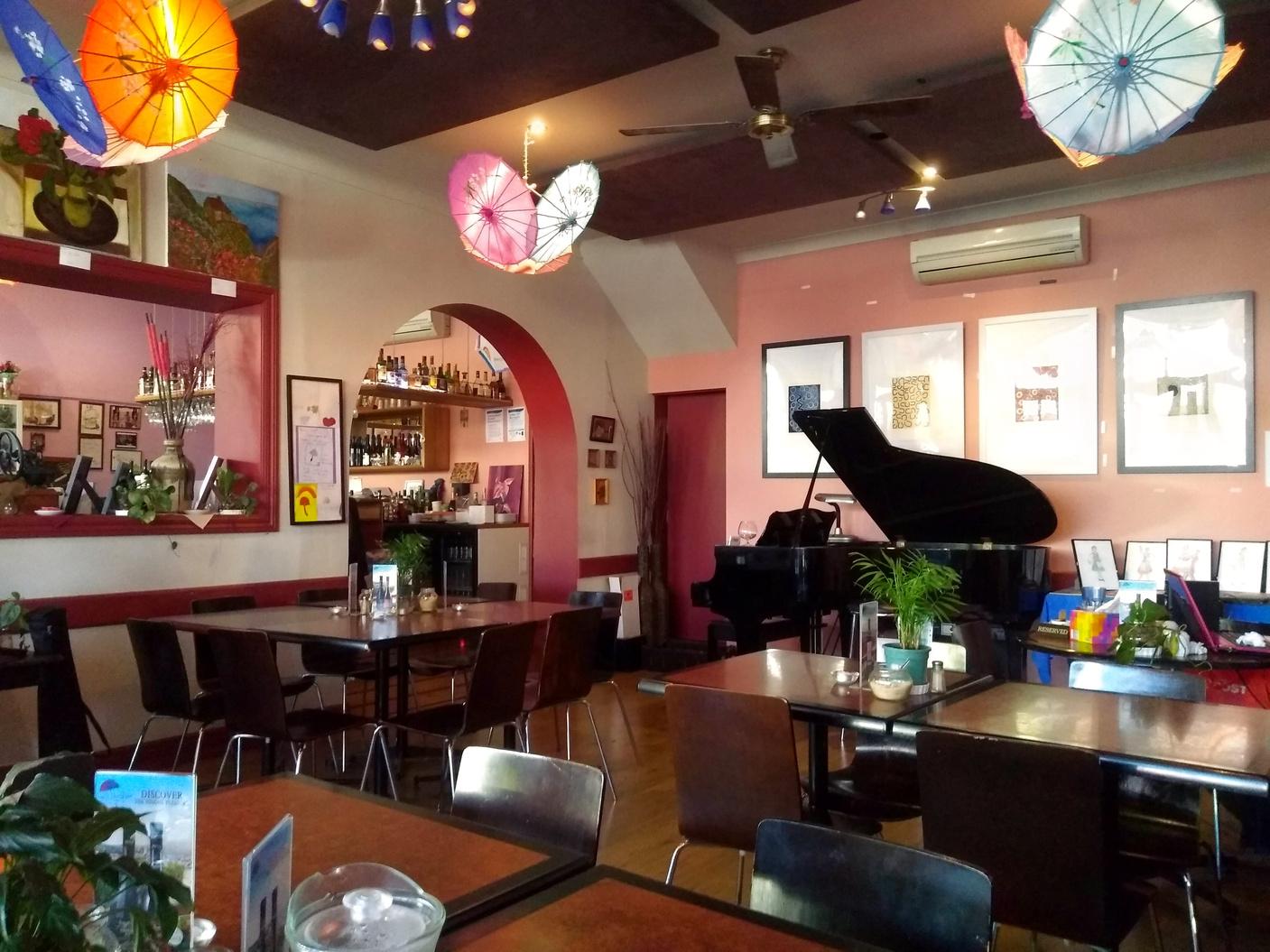 An event space in a bar with colorful umbrella decor, wall art, and a grand piano at Umbrella Lounge Bar.