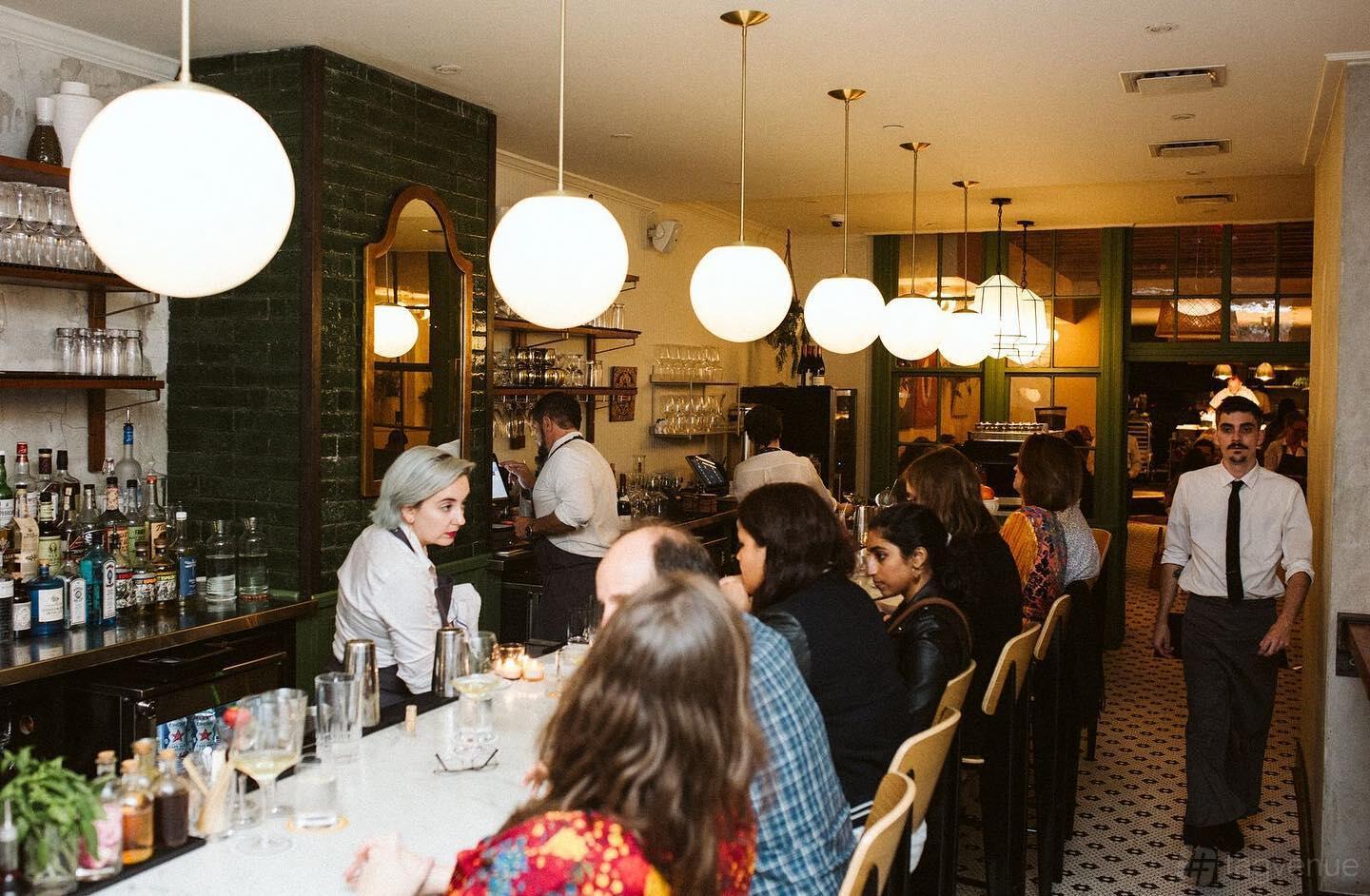 An event space in a restaurant with globe pendant lights, a marble bar, and patrons seated at Forsythia.