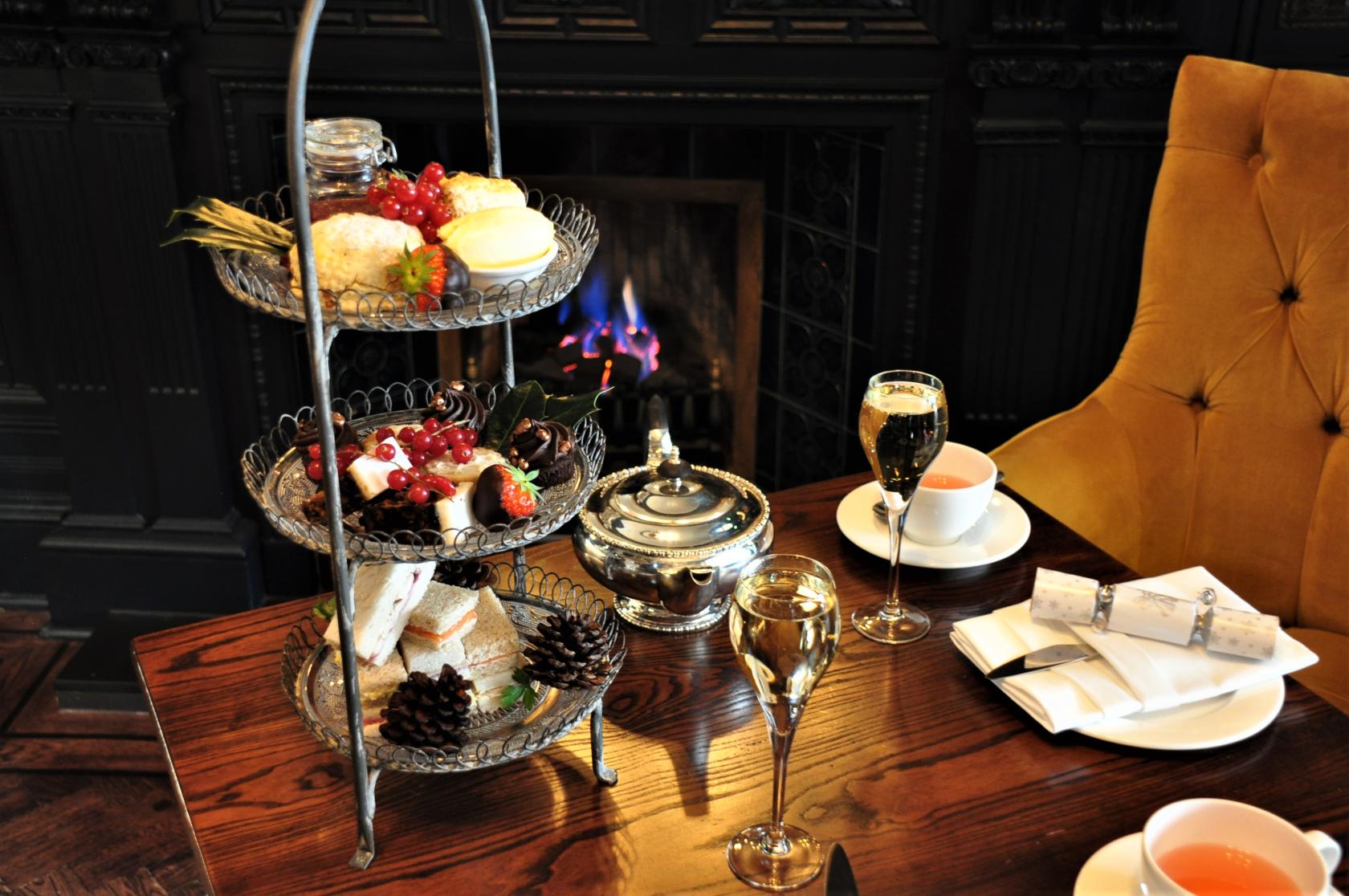 An event space in a hotel with tiered afternoon tea trays, wine glasses, and a lit fireplace at The Roseate Edinburgh.