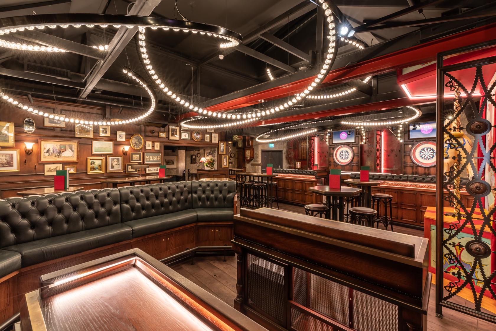 An event space in a bar with leather banquette seating, dartboards, and framed art at Flight Club Islington.