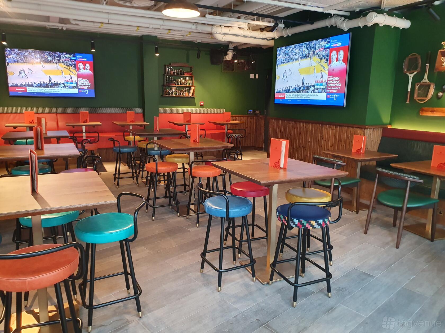 A pub terrace with wooden tables, colorful bar stools, and two large screen TVs at Redwood.