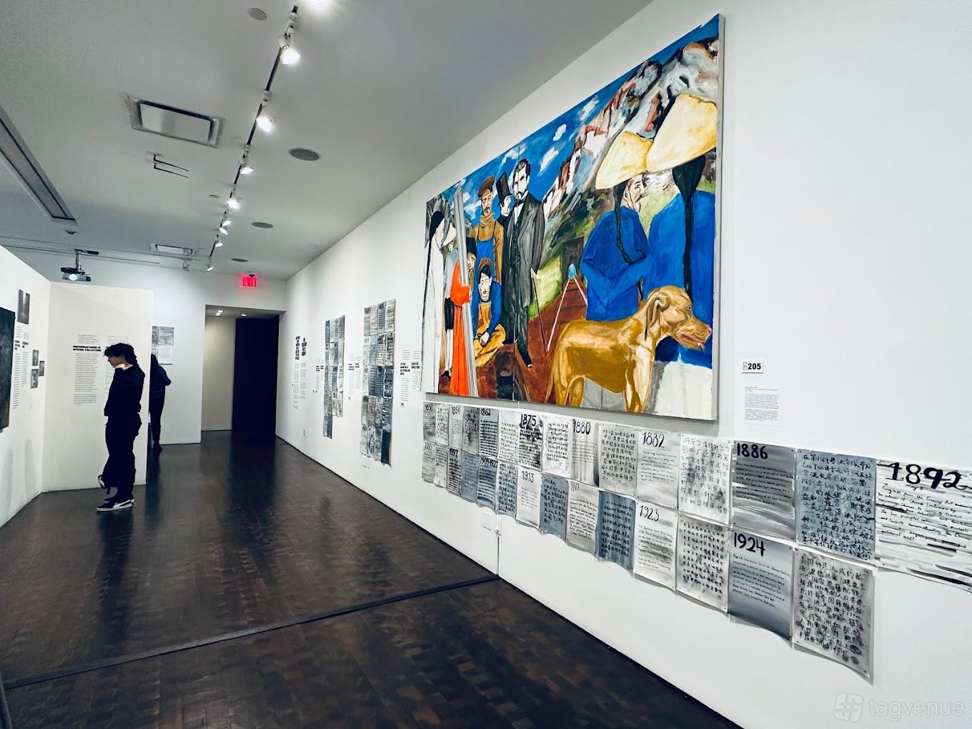 A museum gallery with white walls, wood floors, and a large colorful mural at Museum of Chinese in America.