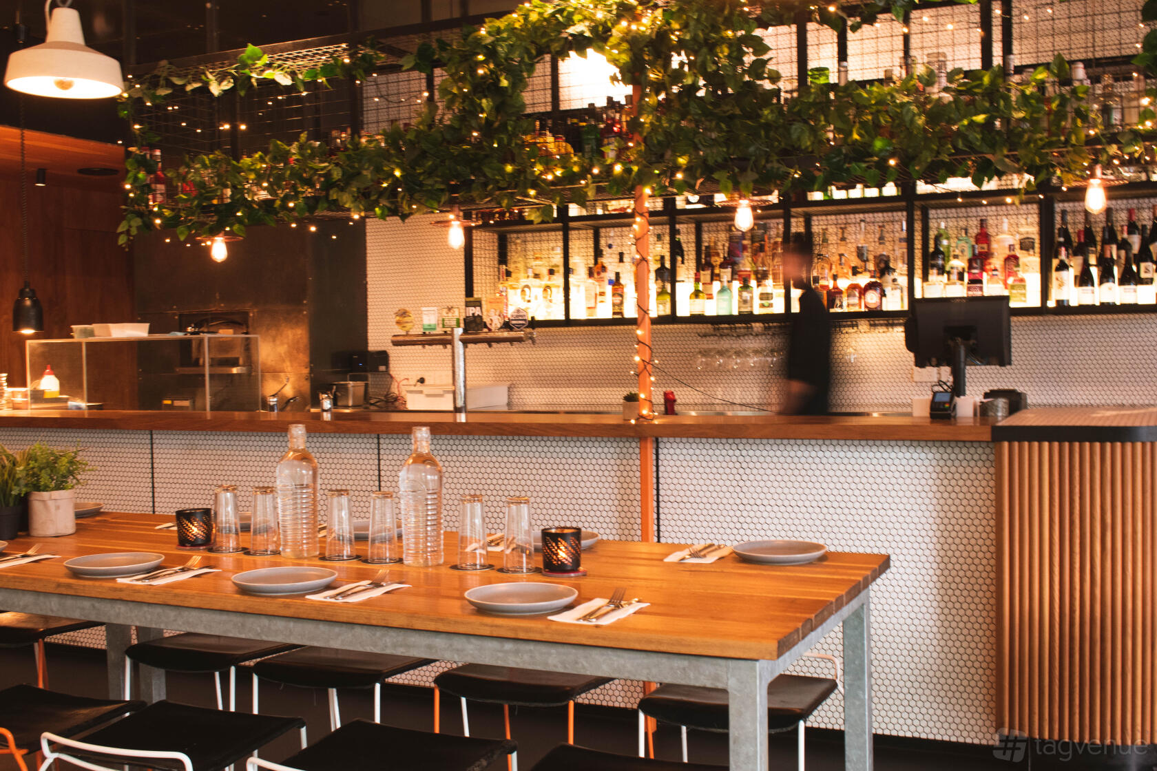 An event space in a restaurant with a long wooden table, hanging greenery, and backlit shelves at BearBrass.