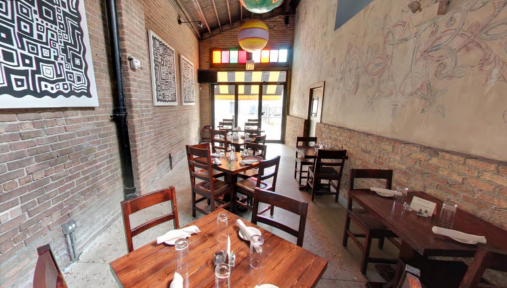 A dining room with exposed brick walls, colorful ceiling lanterns, and wooden tables set for guests at Macello Cucina di Puglia.