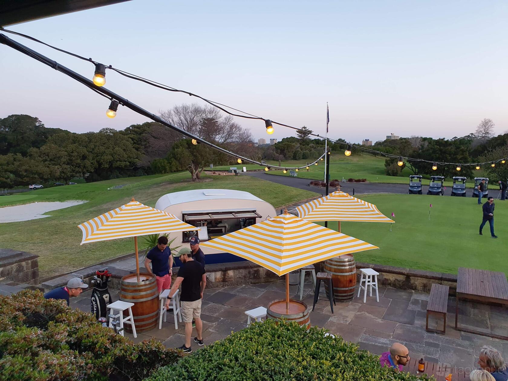 A terrace with yellow striped umbrellas, string lights, and views of the golf course at Moore Park Golf Club.