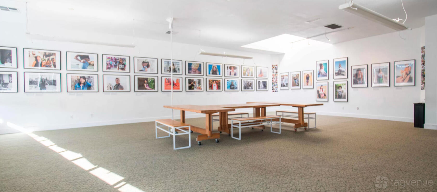 A meeting room with gallery walls displaying framed photographs, skylight, and wooden tables at Oakstop 1721 Broadway.