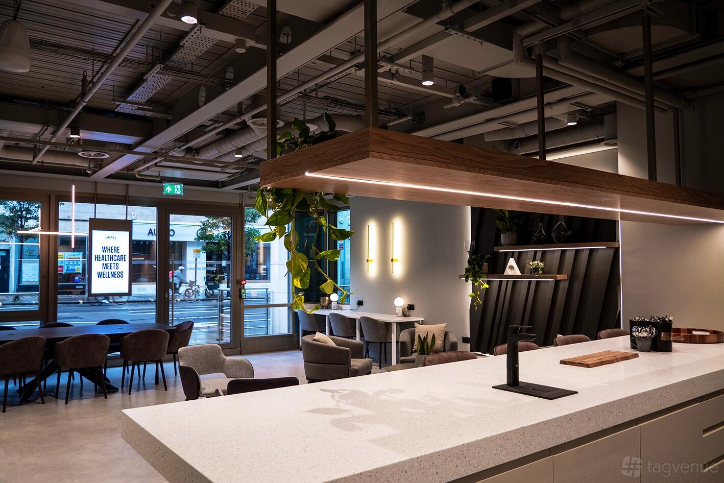 An event venue with a white island countertop, hanging lights, and lounge seating near large windows at Until Marylebone.
