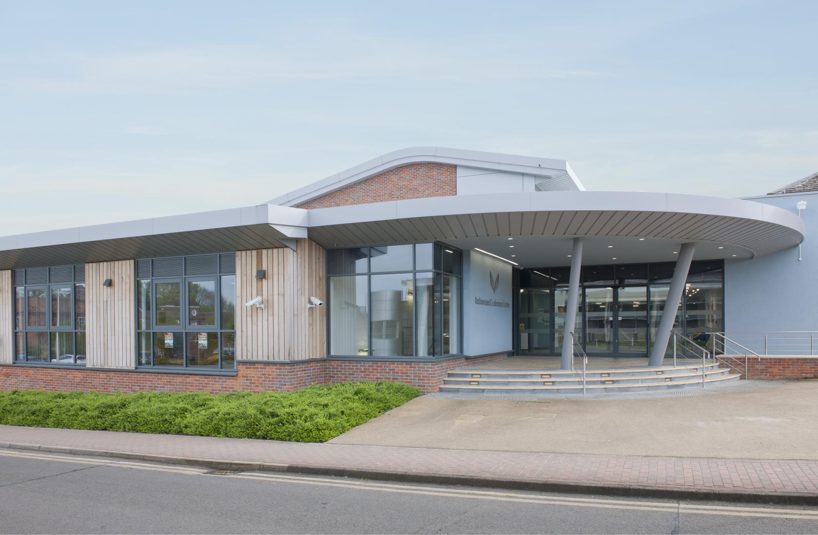 A conference centre with a glass entrance, curved canopy, and brick accents at Rothamsted Conference Centre.