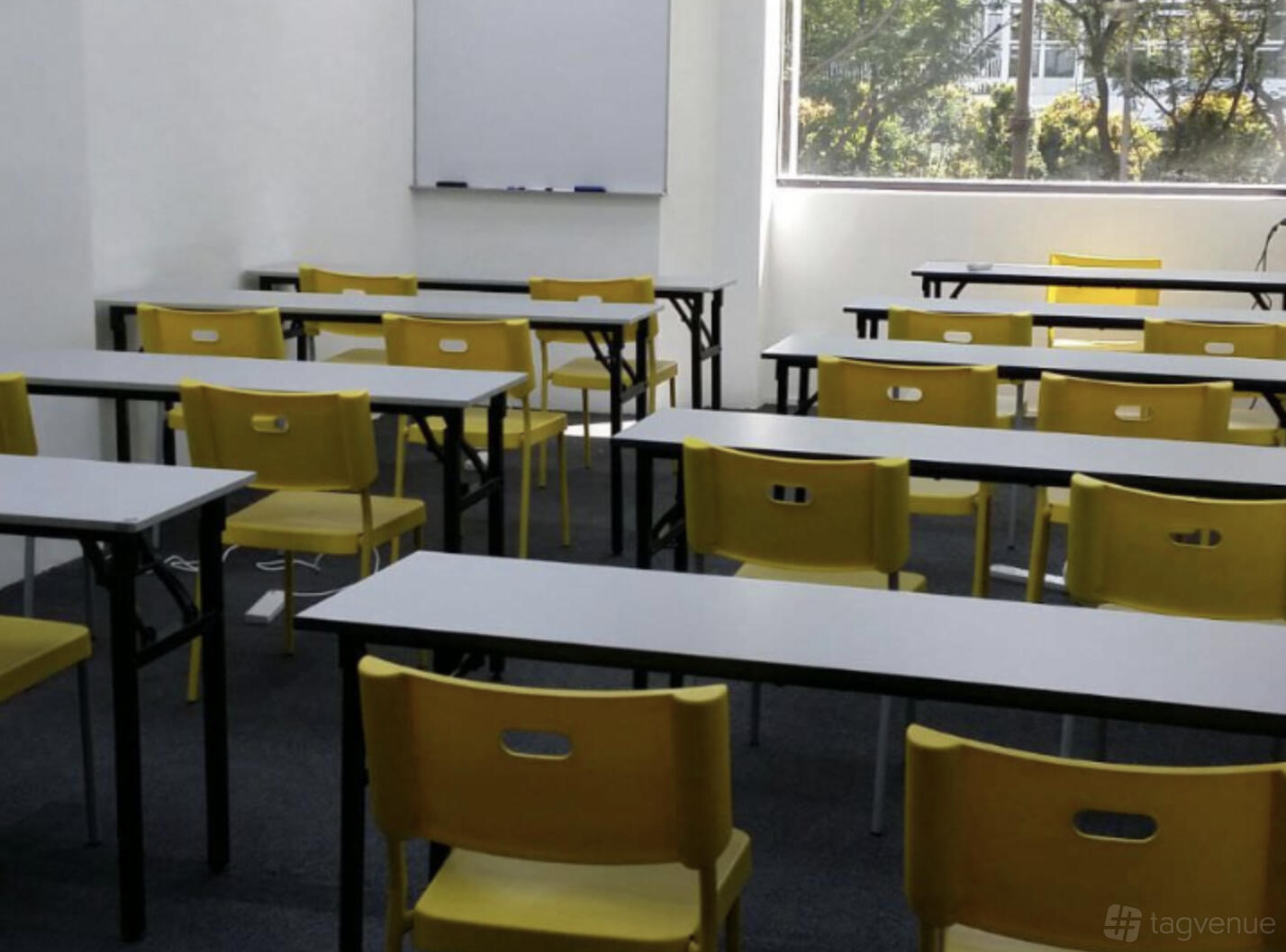 A training room with rows of yellow chairs, white tables, and a whiteboard at Synergy Room Singapore Shopping Centre.