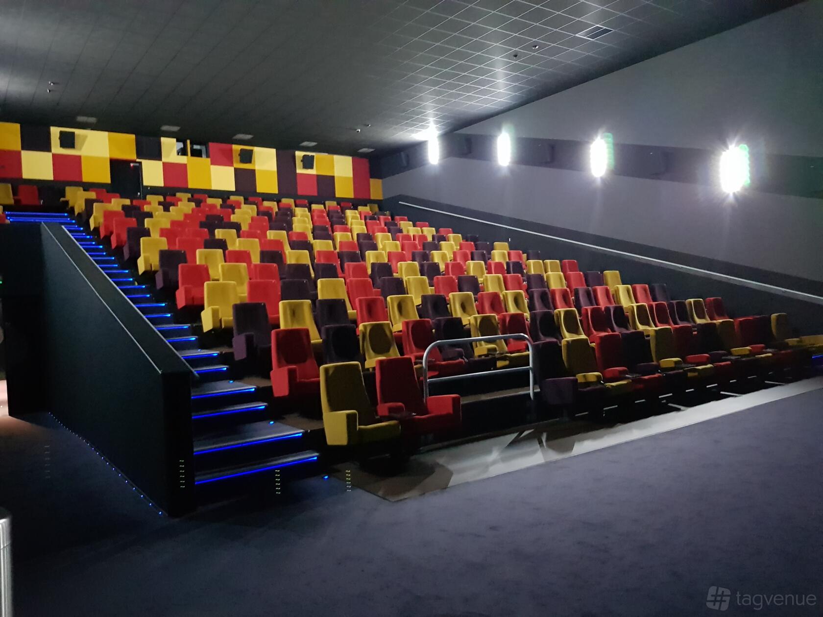 A cinema with tiered seating in red and yellow, illuminated aisle lights, and a large screen at The Light Cinema Bolton.