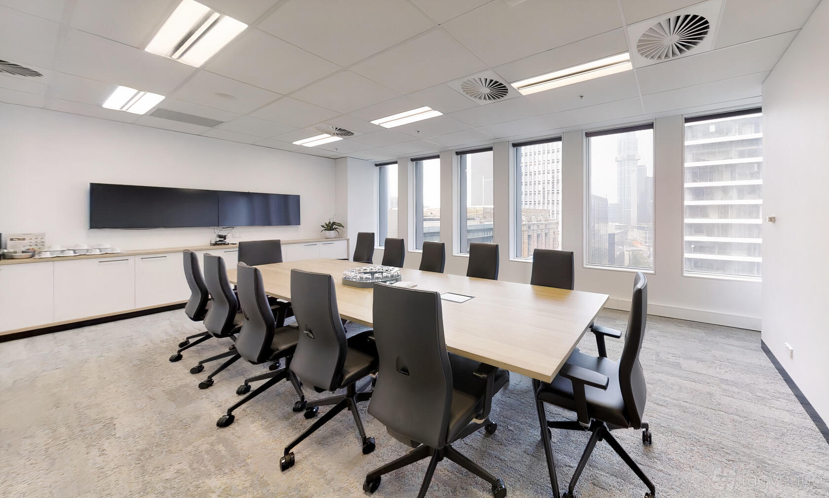 A boardroom with a long wooden table, ergonomic chairs, large windows, and wall-mounted screens at Space Station.
