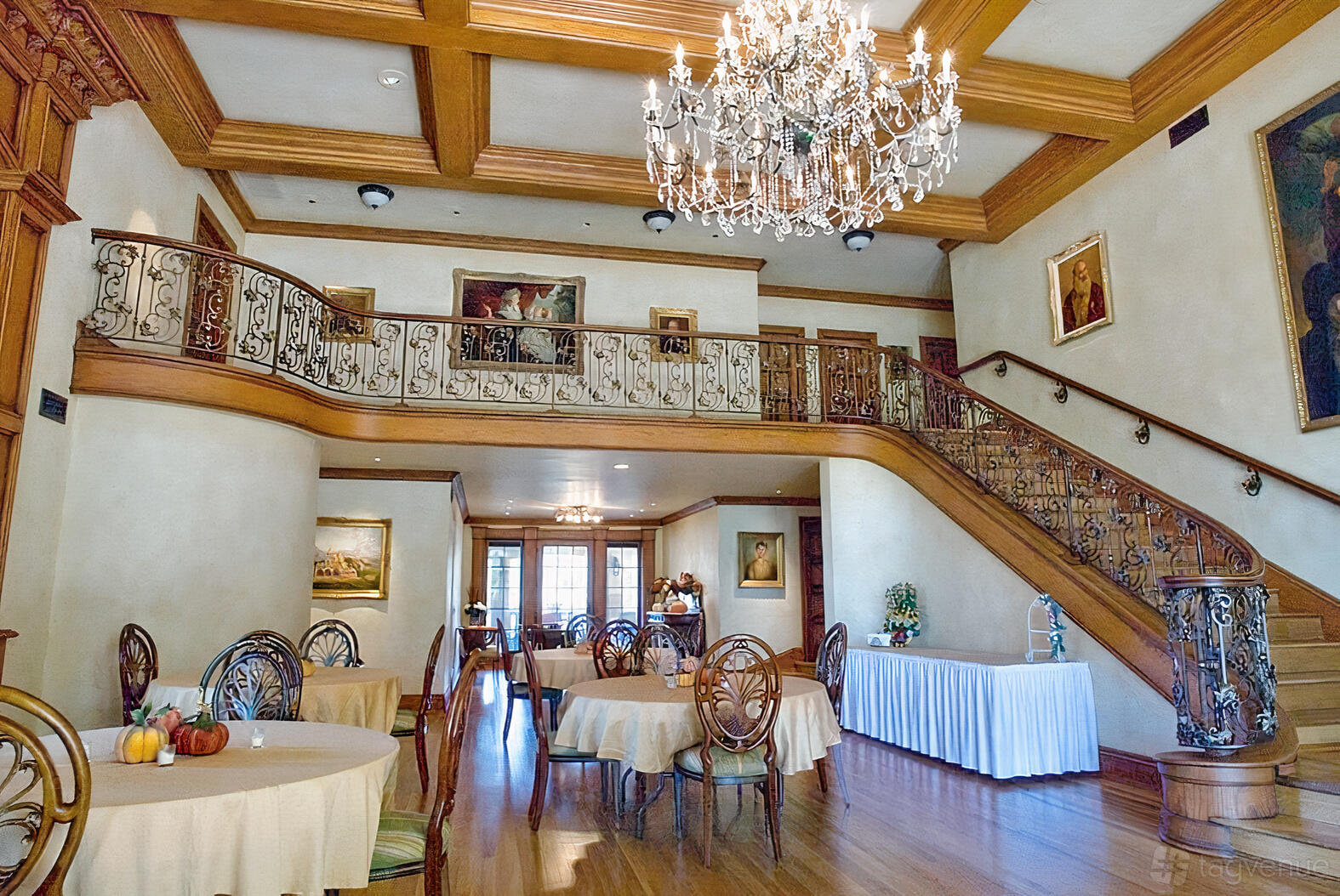 A Mediterranean-style house with a grand staircase, ornate railing, chandeliers, and round tables at Shoot Houses.